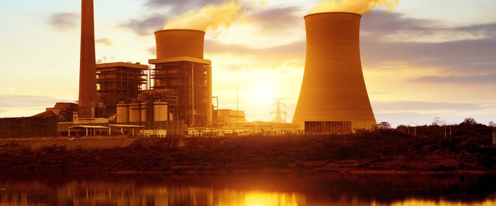 cooling towers backlit by a sunset reflected in a pond